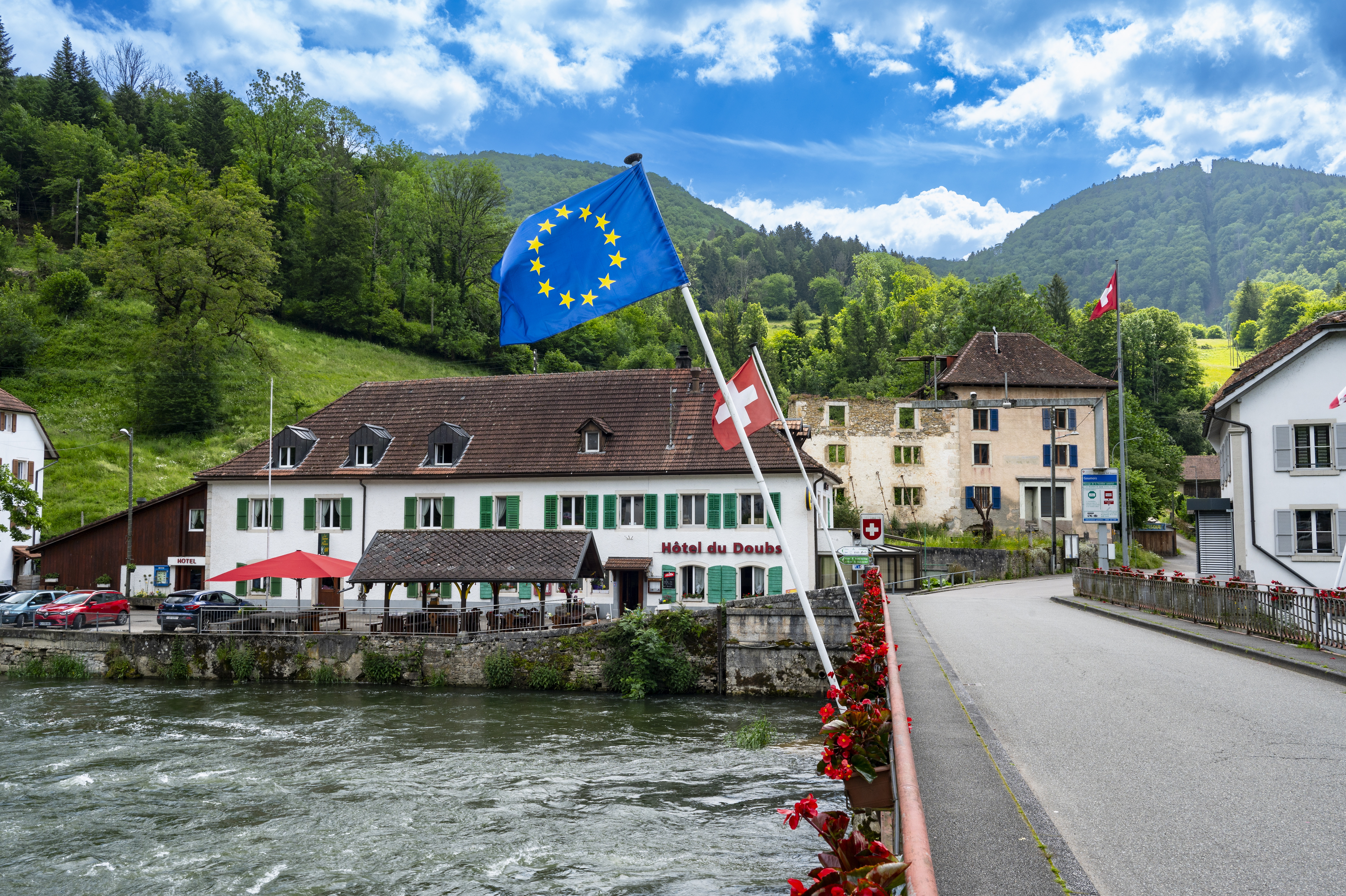 Enjambant le Doubs, le pont activité économique prospère. L’itinéraire offre ensuite une nouvelle opportunité de descente dans la vallée du Doubs. La route en lacets plonge vers Goumois, petit village frontalier à double nationalité. En voiture ou à pied, on passe sans souci de Suisse en France par le pont où flotte le drapeau rouge à croix blanche. Il y a bien longtemps que le bureau de douane est fermé... Goumois a beau vivre avec deux passeports et posséder deux restaurants, un français, l’autre suisse, 