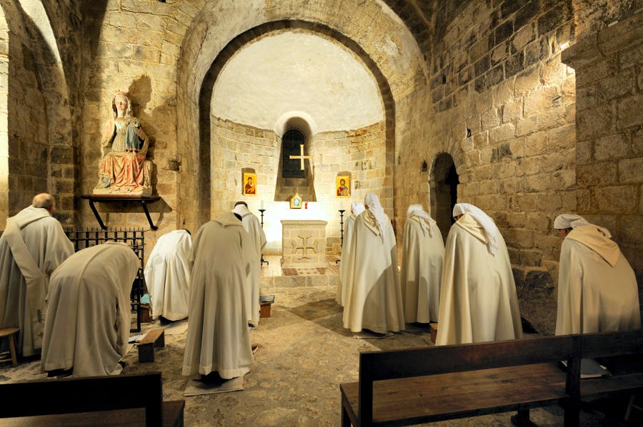 Des moines en prière dans une chapelle en pierre, éclairée par une lumière douce
