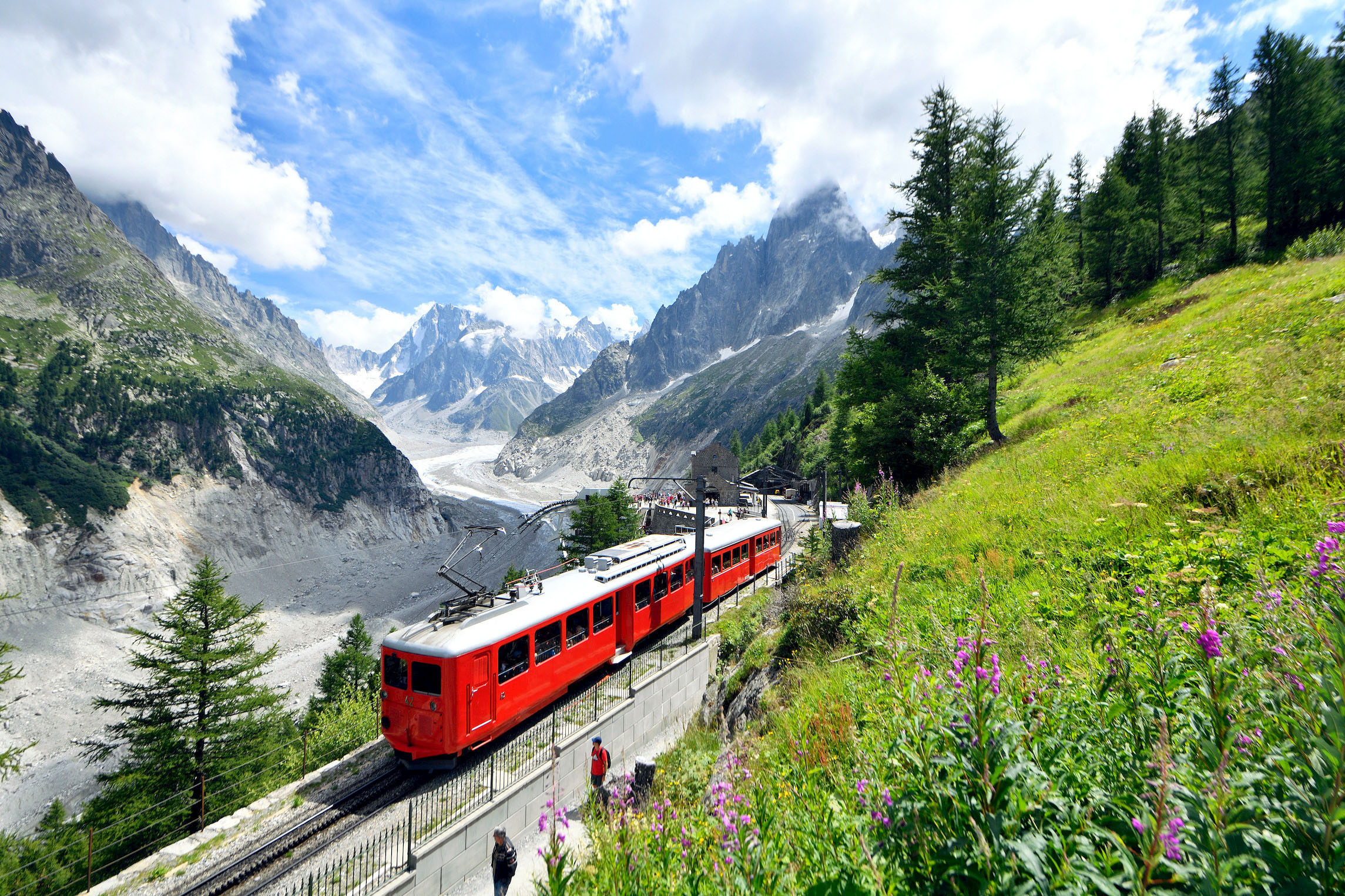 Train rouge traversant les Alpes près de Chamonix, entouré de montagnes et de végétation alpine.